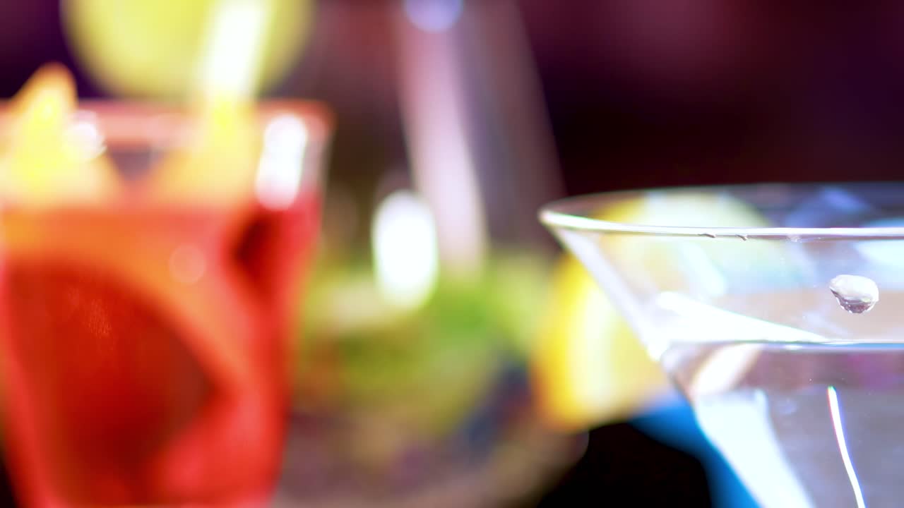 A detailed view of a martini glass with an olive garnish against a blurred, colorful background.