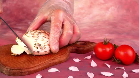 chef hands sliced piece of fresh mozzarella with a kitchen knife on cutting board, tomatoes.