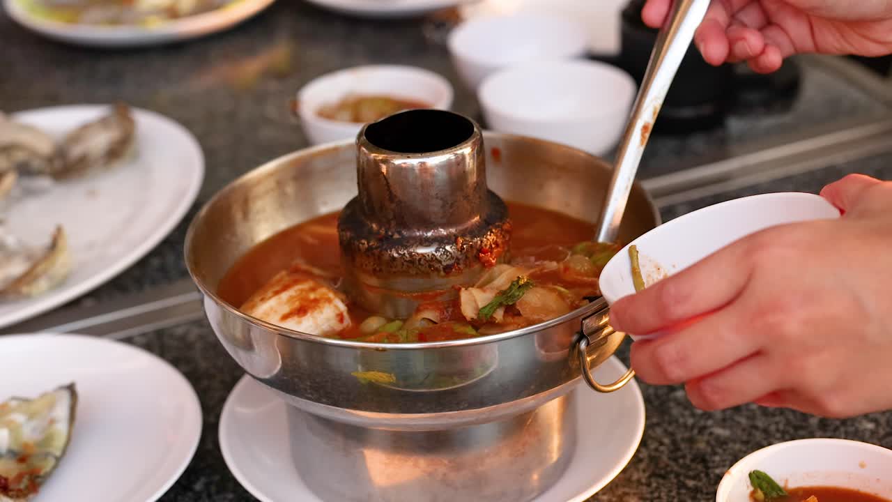 Hands serving soup from a hot pot