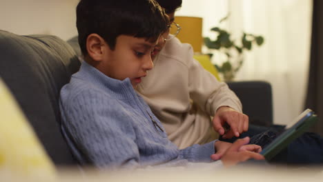 two young boys sitting on sofa at home playing games or streaming onto digital tablet 2