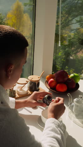 el marido mezcla hojas de té secas en un frasco de vidrio. el hombre experimenta con hacer té natural durante la comida de la mañana. beneficios para la salud de los ingredientes naturales