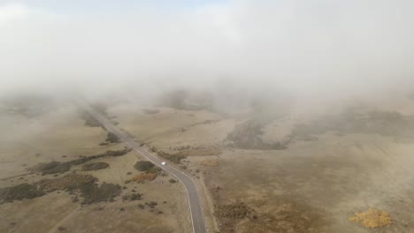 White-car-drive-countryside-road-into-fog,-Madeira,-Portugal,-aerial