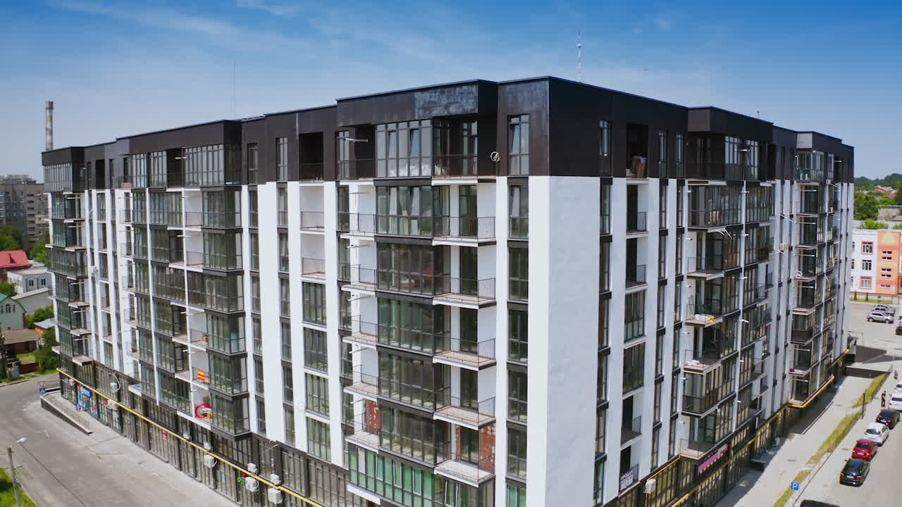 Multi-storey building in white and black colors. Exterior of a tall newly built residential apartment building with many windows and balconies. Camera moving down.