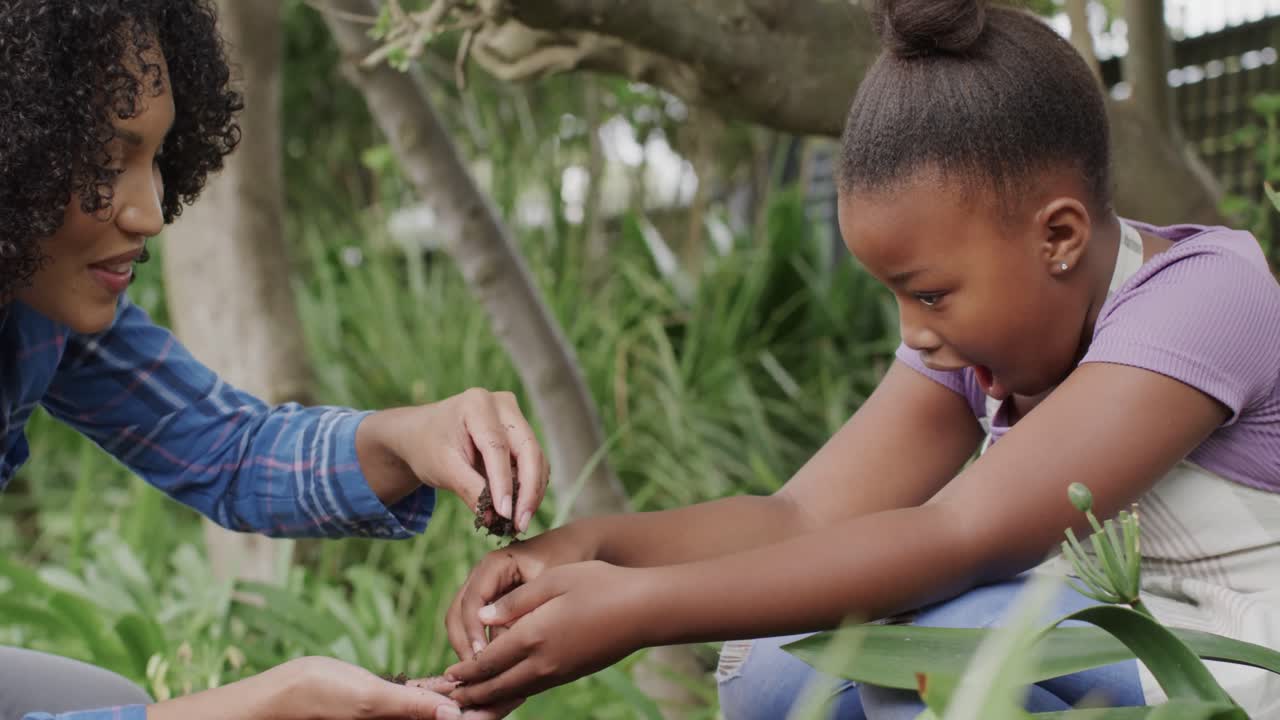 madre y hija afroamericanas felices tocando el suelo en el jardín, en cámara lenta.