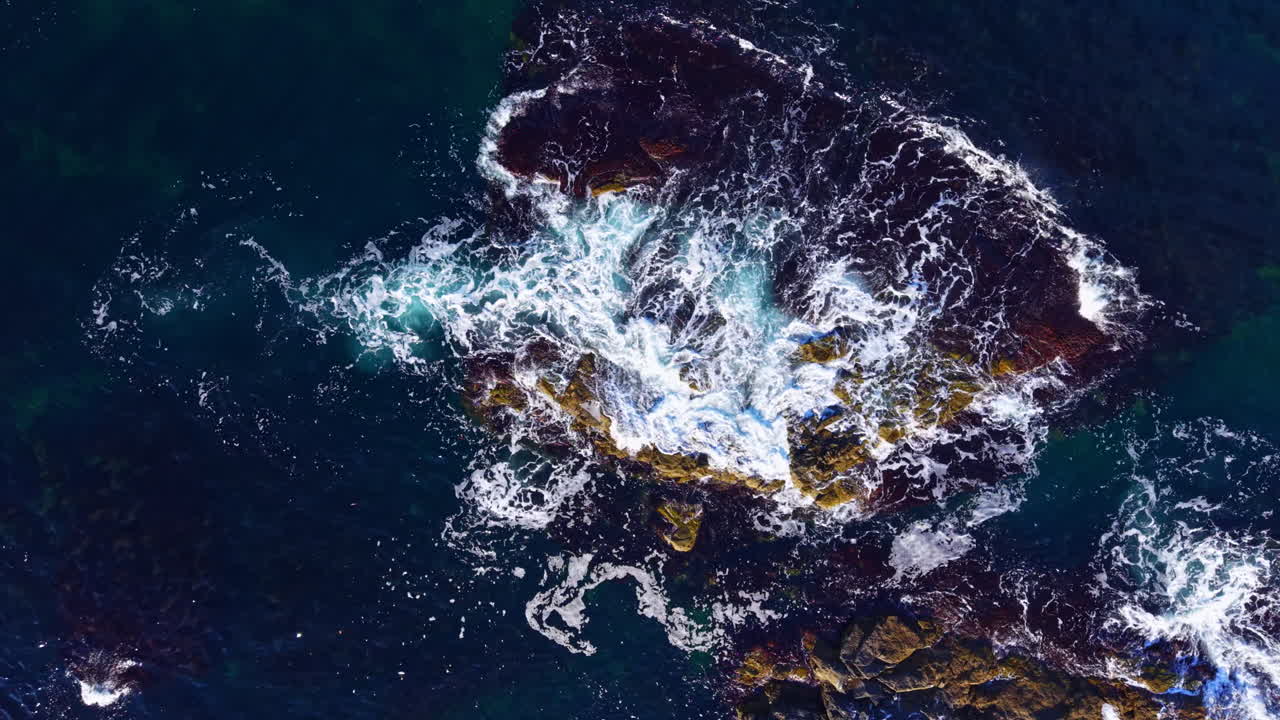 Majestic waves crashing against rugged rocks at sunset along a serene coastal landscape with deep blue waters