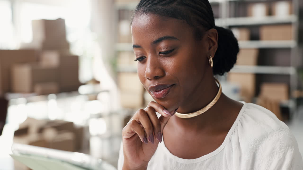 Young Black Woman Thinking While Working on Tablet in Warehouse