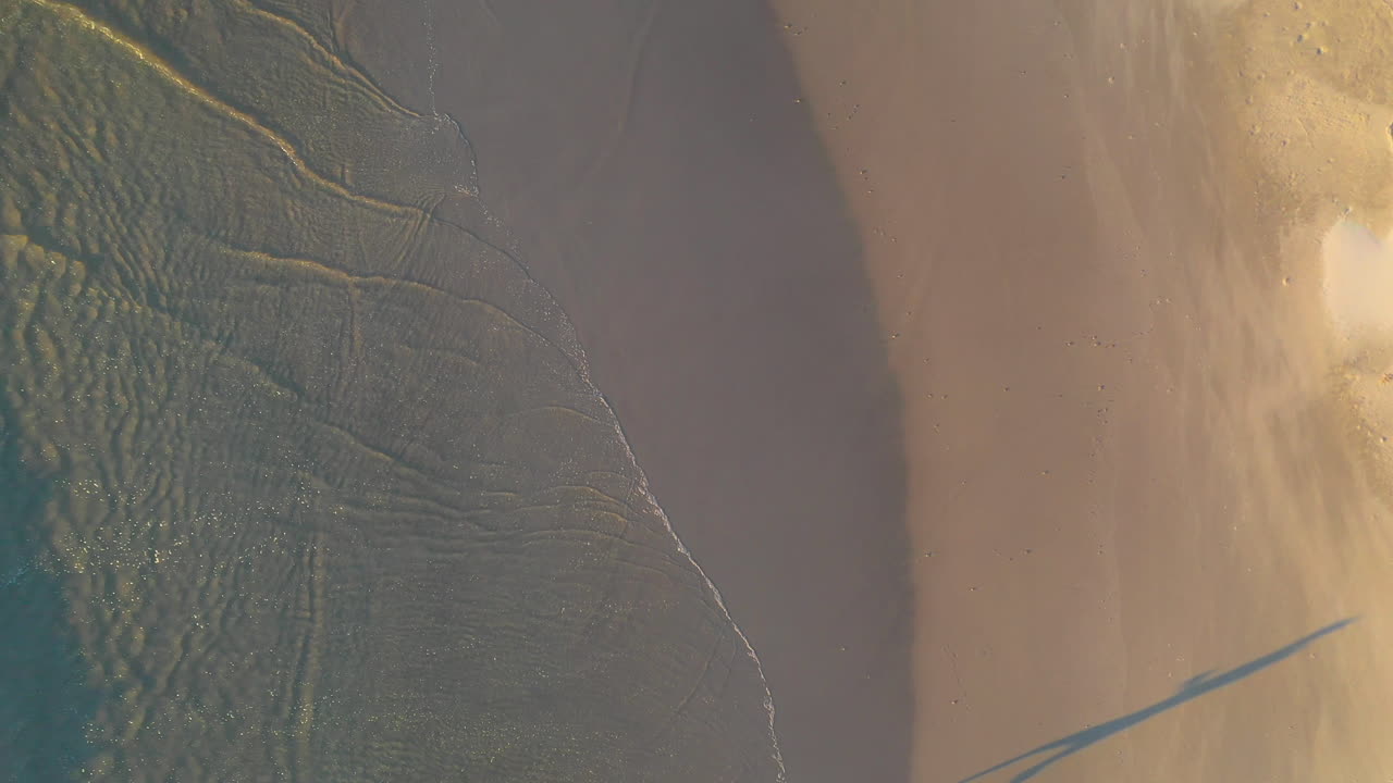 disparo de drones hacia abajo de una persona corriendo en una playa de arena con la cabeza rota cerca de byron bay