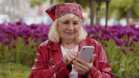Senior woman use smartphone typing text messages browsing internet finishing work looking at camera