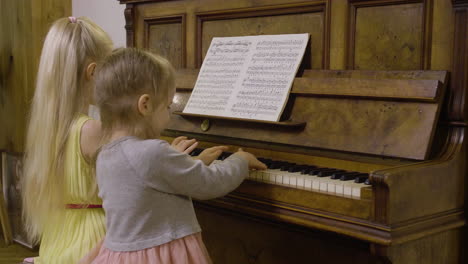 side view of two little girls playing old piano at home 1