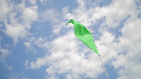 low angle of a green flag on the beach waving in slow motion