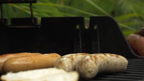 Barbacoa-Día-Soleado-Salchichas-Comida-A-La-Parrilla-Hombres-Colocando-Salchichas-En-La-Barbacoa-Fuego-Cocina-Cruda-Despegando-Comida-Lista