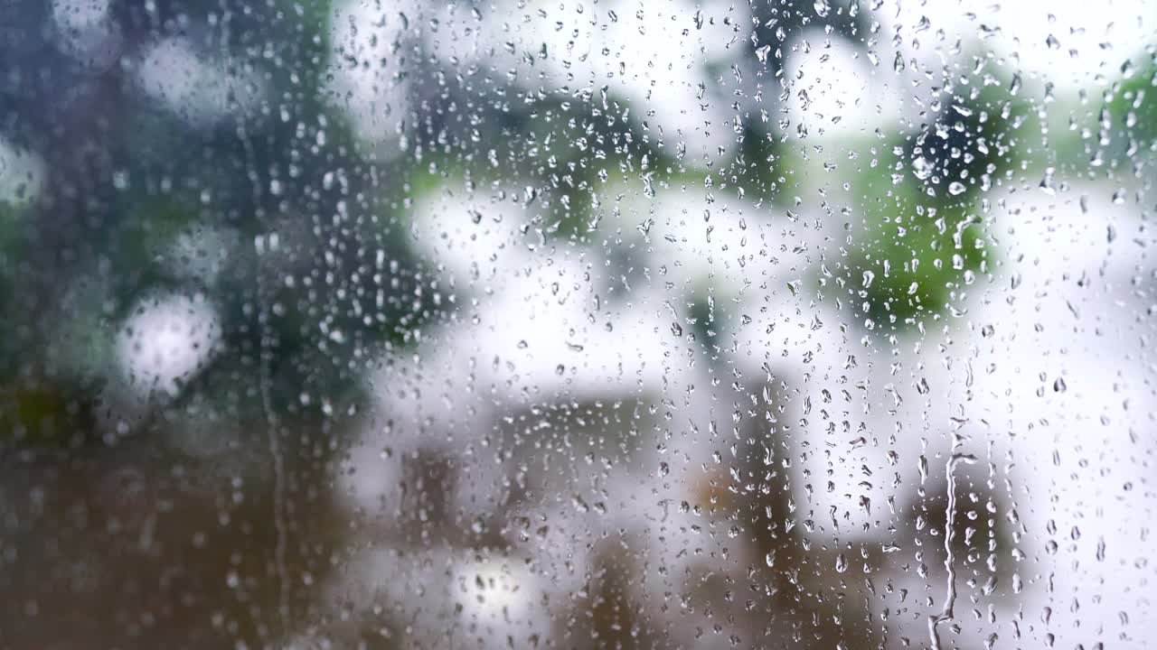 4k : Close-up of rain drops splashing against a window glass with light leaks.