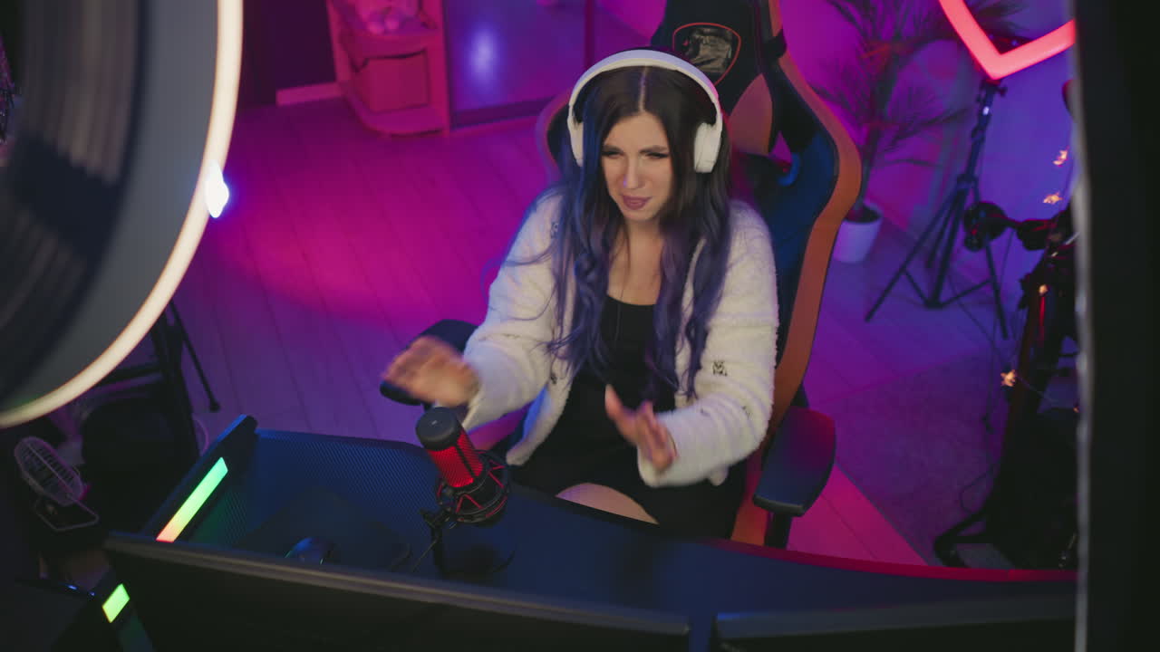 Top view of woman in headphones leaning back in chair showing frustration while working on digital project in vibrant studio setup, surrounded by tech equipment including microphone and ring light