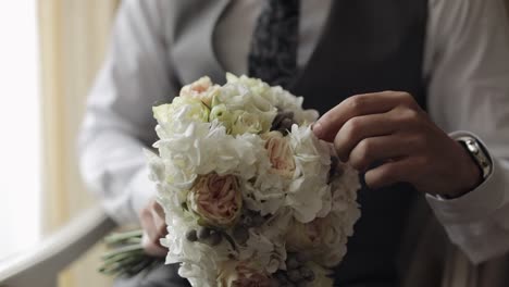 Groom-with-wedding-bouquet-in-his-hands-at-home-preparing-to-go-to-bride,-close-up-slow-motion