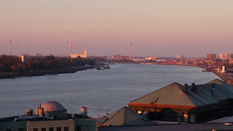 Time-lapse-video-of-the-River-Scheldt-in-the-city-of-Antwerp,-Belgium-with-many-boats-cruising-by-the-river-and-the-ferry-transporting-people-from-one-side-of-the-river-to-the-other-side-at-sunset