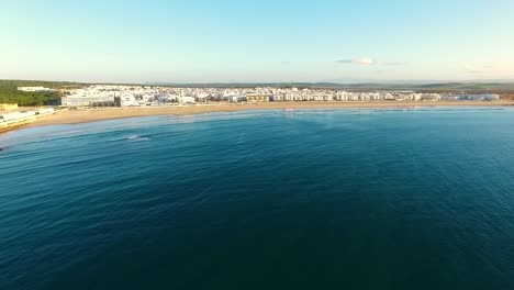 toma aérea de la costa con un pueblo de casas blancas, día soleado y pequeñas olas en el mar