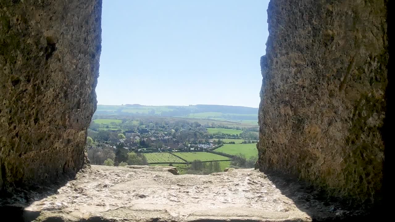dentro de los restos estructurales del castillo de corfe, con la vista pov vista a través de la ventana que muestra el campo y una pequeña granja