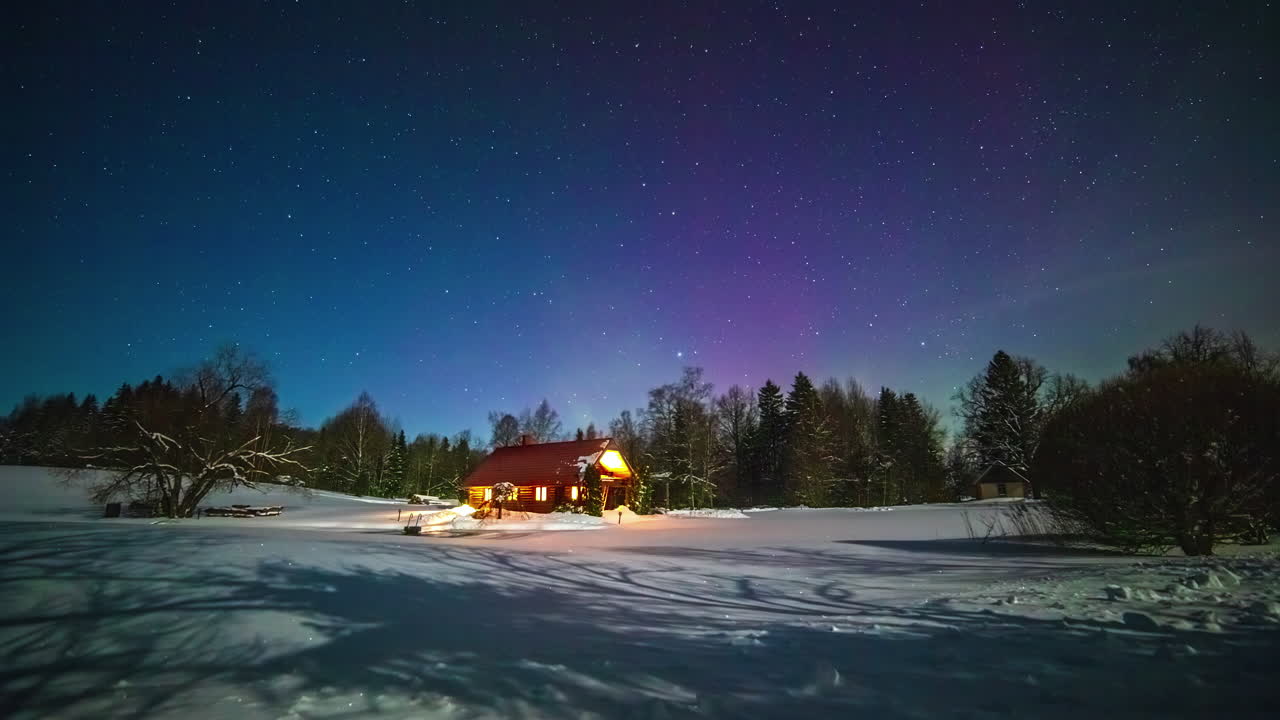 aurora boreal y vía láctea en el cielo con nubes sobre un paisaje nevado con árboles y una casa de madera con luces cálidas