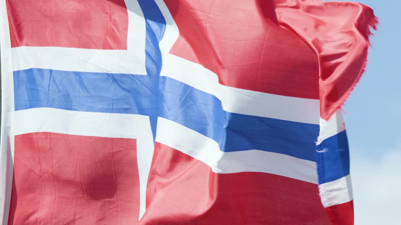 Close-up views of the Norwegian flag fluttering dynamically in the wind against a clear blue sky, captured with natural daylight and smooth camera tracking