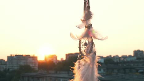 amulet dreams boho style catcher waving in light wind against backdrop of bright sunset and bokeh of city lights. white light feathers rise in wind. disc of the setting sun. ethnic amulet