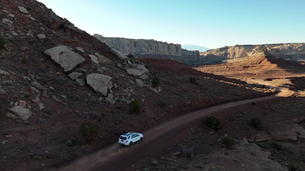 Ripresa aerea con drone di un SUV bianco in movimento su una strada desertica in un paesaggio desertico arido dello Utah, USA.