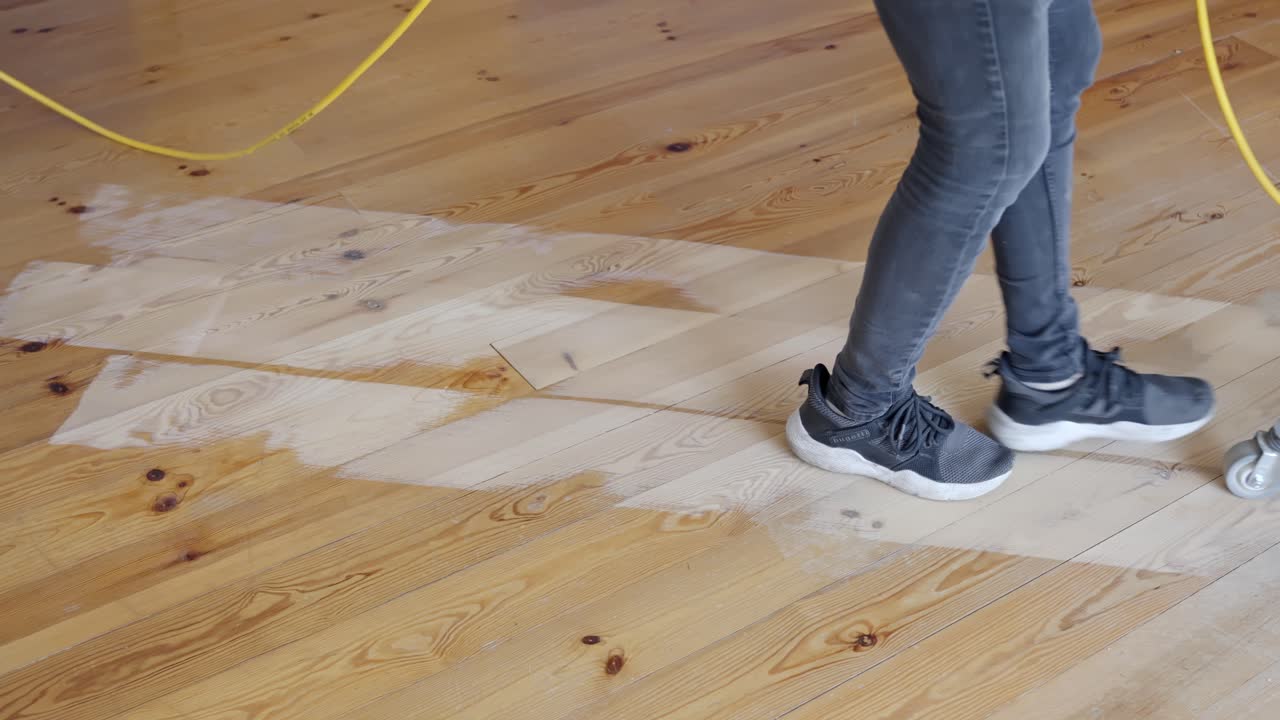 Man sanding pine floor with machine, removing old finish to reveal smooth surface