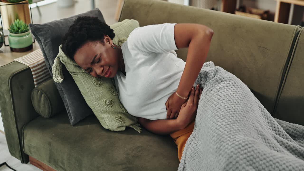 Woman experiencing abdominal pain on a couch