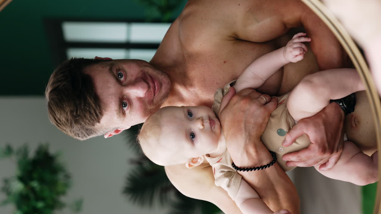 Happy dad holding his beloved baby in front of a mirror. Loving father with son family portrait. Vertical screen.