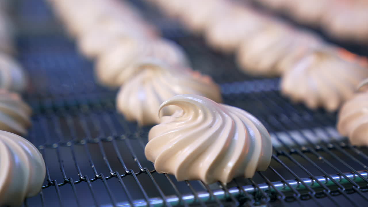 Creamy marshmallows move on the conveyor belt. Savory whipped cream desserts manufactured by modern food factory. Close up. Blurred background.