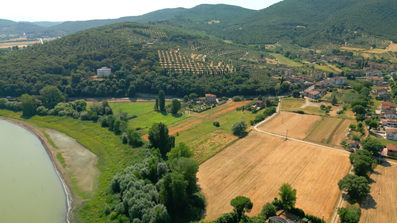 Beautiful aerial view of lake trasimeno coastline, showcasing cultivated fields, olive groves, and a small village nestled amidst the picturesque landscape of umbria, italy