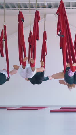 slim women group relaxes after modern fly yoga exercise and swing on long bright red hammocks in pilates room