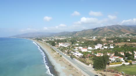 Chrysochous-bay-in-cyprus,-showcasing-serene-beachfront-and-lush-hills-under-blue-skies,-aerial-view