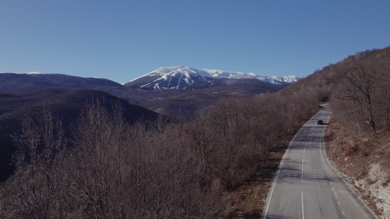 coches que pasan por una carretera de montaña con una montaña nevada al fondo