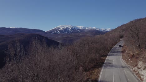 cars passing by a mountain road with a snowy mountain in the background