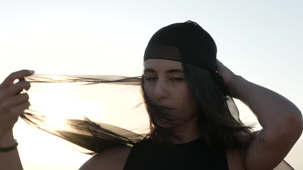 백라이트에 태양과 검은 투명 목도리로 그녀의 얼굴을 덮고 젊은 여자