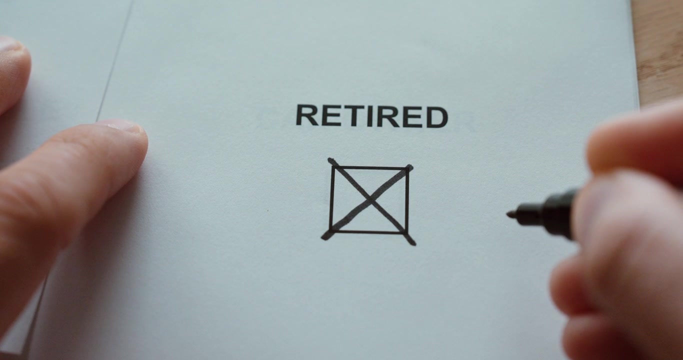 Close-up of a hand drawing a cross in the retired status checkbox on a paper form.