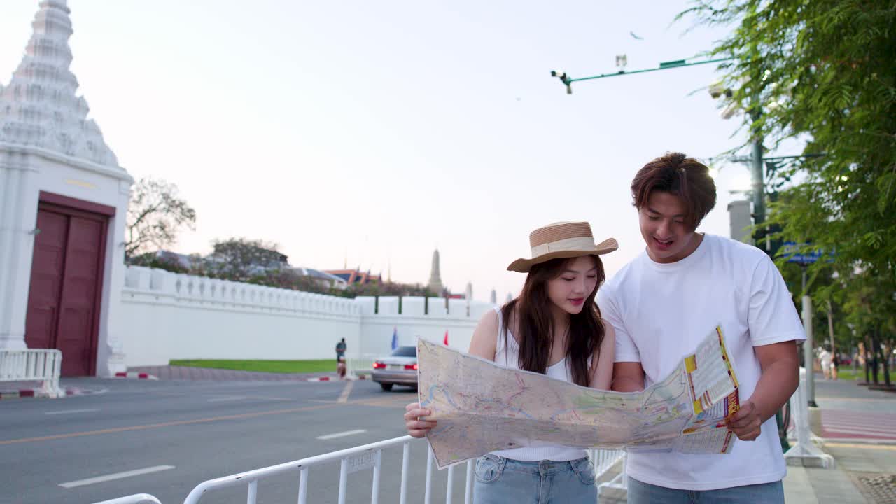 Asian couple consults map together outdoors, soft sunset lighting, temple background, gentle camera movement