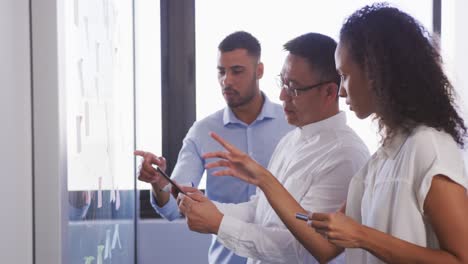 Senior-businessman-with-digital-tablet-discussing-with-young-business-people-over-memo-notes