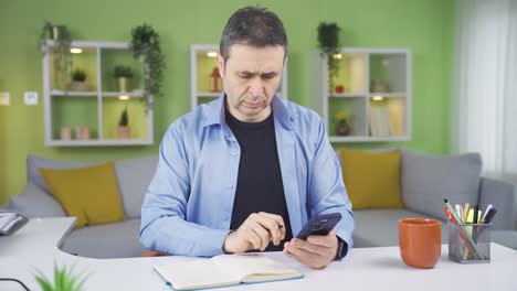 Man-taking-notes-in-notebook-while-looking-at-phone.