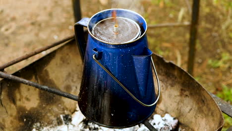 blue enamel coffee pot on fire at campsite - percolated coffee, close up