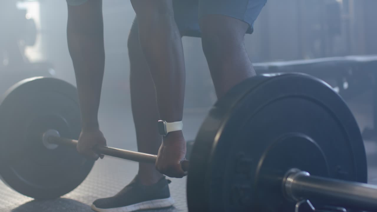 African male training duo bracing gripping and pulling barbell at gym, spotter steadying with watch