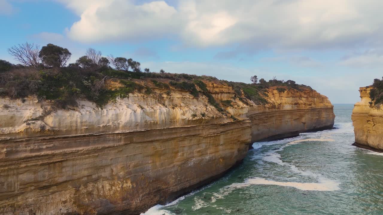 Drone footage captures the dramatic cliffs and ocean waves at Loch Ard Gorge, Port Campbell, under soft daylight
