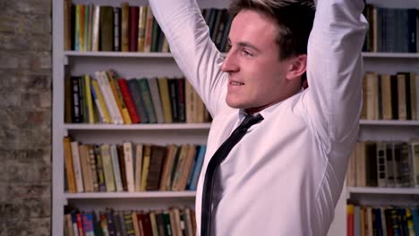 young happy businessman is keeping hands fist, raising hands up, gesture concept, bookshelf on background