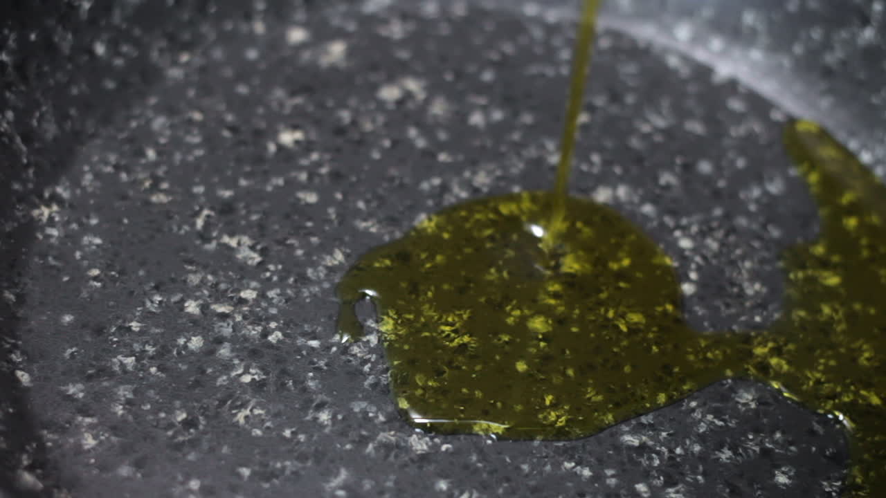 капание оливкового масла на черно-белую сковороду с антипригарным покрытием, крупный план