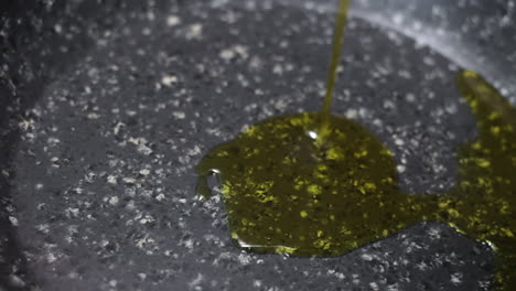 Drizzling-olive-oil-in-speckled-black-and-white-nonstick-pan,-close-up