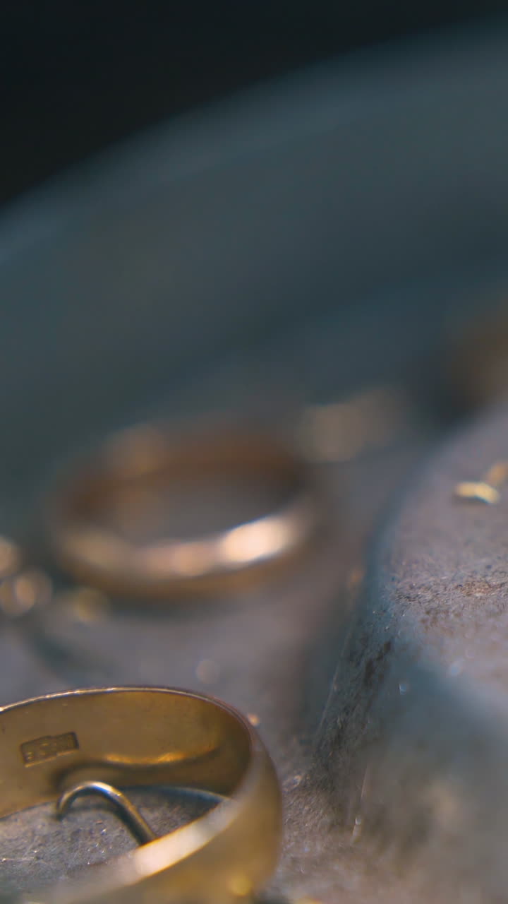 CU shot: little parts of cut excess gold chain falls down into metal box with wedding rings and yellow shavings close view