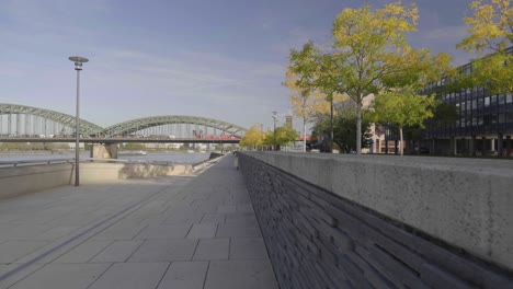 dolly forward shot of a pedestrian walkway along the rhein treppen, close to a stone ledge with trees, bridge, and cityscape in the background, slow motion, cologne germany