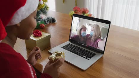 Mujer-Afroamericana-Con-Gorro-De-Papá-Noel-Usando-Una-Computadora-Portátil-Para-Una-Videollamada-Navideña,-Con-La-Familia-En-La-Pantalla