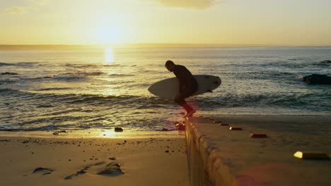 vista lateral de un surfista caucásico adulto caminando con una tabla de surf en la playa 4k