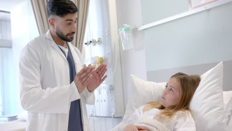 diverse male doctor with asthma inhaler explaining to girl patient in hospital bed, slow motion